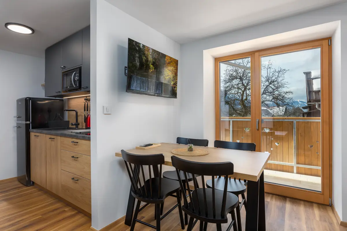 Profesionalna fotografija jedilnega kota in moderne kuhinje v apartmaju, ki z razgledom na gore skozi okno ustvarja domačnost in poveča število rezervacij.