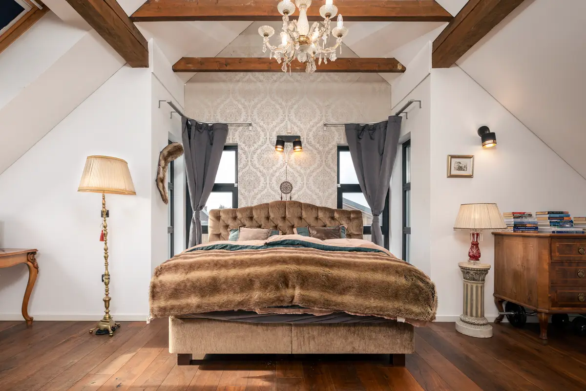 Profesionalna fotografija luksuzne glavne spalnice v mansardi, ki z izpostavljenimi tramovi in edinstvenim stilom nagovarja zahtevne kupce ter ustvarja vtis prestižne nepremičnine.