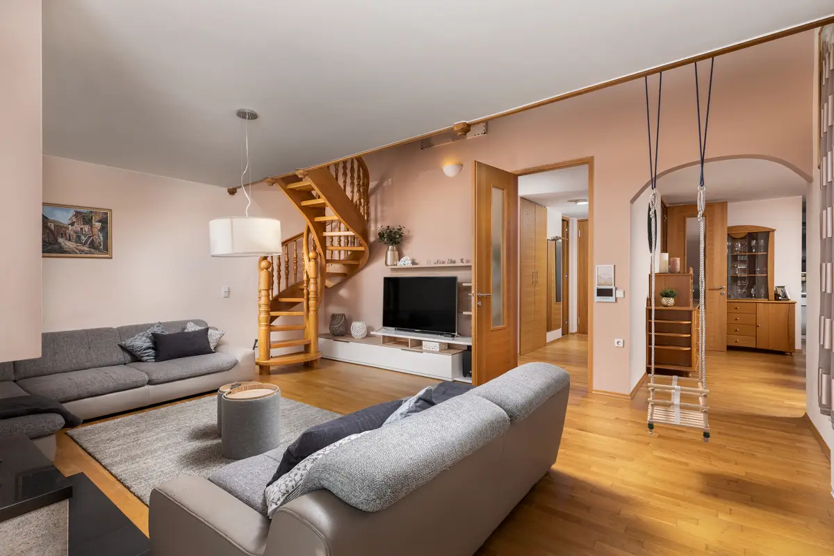 Profesionalna fotografija prostorne dnevne sobe v družinski hiši ali dvoetažnem stanovanju, ki poudarja odprtost prostora, lesene polžaste stopnice in občutek domačnosti, kar privablja družine.