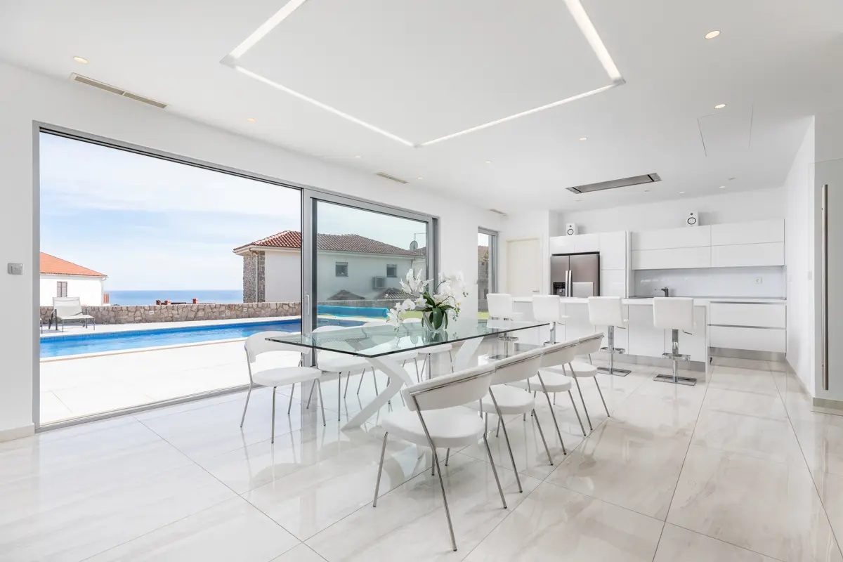 Fotografija, ki prikazuje sanjski pogled na morje iz moderne, z belino obsijane jedilnice in kuhinje, gostom obljublja ekskluzivno doživetje in je glavni razlog za takojšnjo rezervacijo.