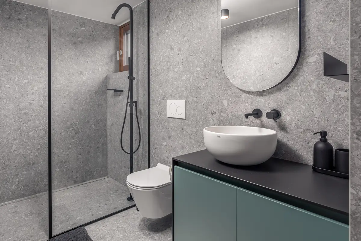 Portfeljska fotografija kopalnice, ki prikazuje sodobne trende v notranjem oblikovanju: uporabo teraco keramike v kombinaciji z mat črnimi armaturami in pohištvom v barvnem poudarku.