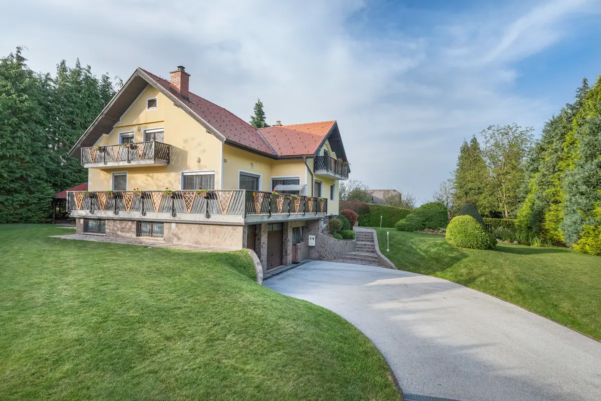 Profesionalna fotografija prostorne samostojne hiše z veliko, urejeno zelenico in dovozom, ki poudarja privlačnost nepremičnine za potencialne kupce.